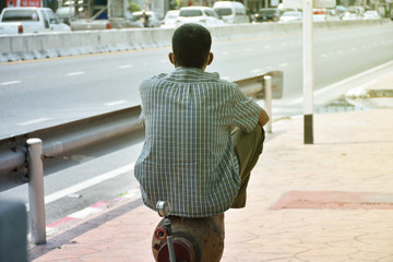 Backside of asian man sitting alone on fire hydrant on the sidewalk and looks as though he is...