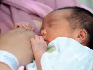 A newborn little girl is sleeping in her mother's chest and touching her mother's finger. She looks so adorable, cute, comfortable, and safety.