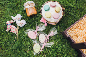 Obraz na płótnie Canvas Easter wooden basket on grass. Contents: Easter cake, gingerbread cookies decorated with glaze, a jar of caramel, handmade toys: rabbit, birds