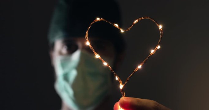 Occhi in primo piano di un medico in prima linea alla lotta al Coronavirus tiene in mano un piccolo simbolo del cuore luminoso per dare speranza alla fine della pandemia Coroanvirus.