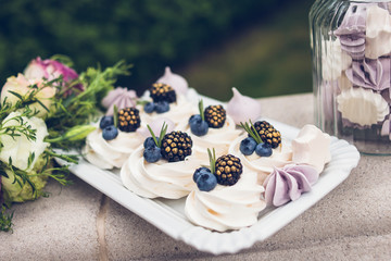 Meringue cake is decorated with blackberries and blueberries lying on the spacing, next to the flowers. Candy bar. Wedding reception. 