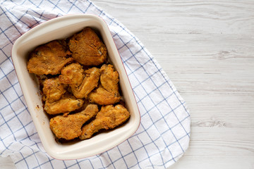 Crispy homemade oven baked fried chicken in a dish on a white wooden table, top view. Flat lay, overhead, from above. Space for text.