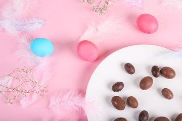 Happy Easter. Congratulation easter pink background. Easter pastel eggs with chocolate eggs on plate decorated with pink feathers. Style concept. Top view, flat lay, mockup