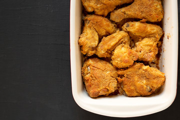Delicious homemade oven baked fried chicken in a dish over black surface, top view. Flat lay, overhead, from above. Space for text.