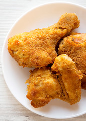 Homemade tasty oven baked fried chicken on a white plate on a white wooden table, top view. Overhead, from above, flat lay.