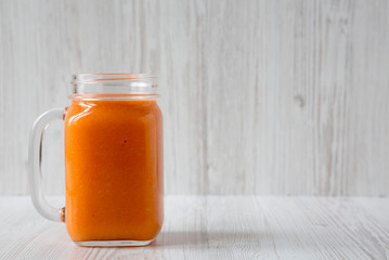 Homemade Mango Carrot Smoothie in a glass jar mug over white wooden surface, side view. Copy space.