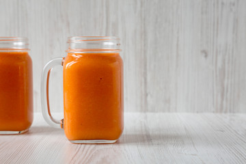 Homemade Mango Carrot Smoothie in a glass jar mug over white wooden surface, side view. Copy space.