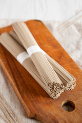 Uncooked Buckwheat Soba Noodles on a rustic wooden board on a white wooden table, low angle view. Close-up.