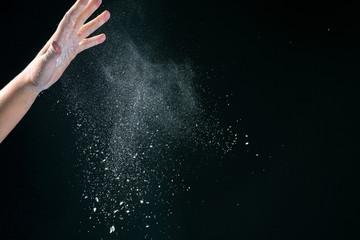 Obraz na płótnie Canvas Hand of european woman chef in kitchen pouring flour on black background