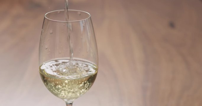 Slow motion pour white wine in wineglass on walnut table