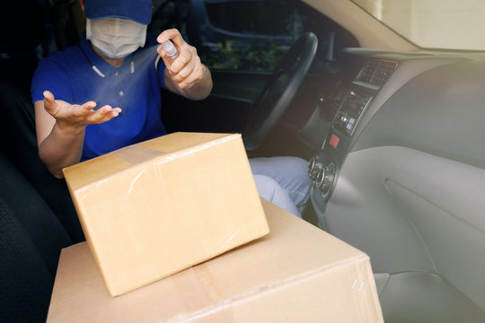 Safety delivery service courier during the Coronavirus (COVID-19) pandemic, courier driver wearing medical protective mask spraying alcohol disinfectant spray on hands over cardboard boxes in van.