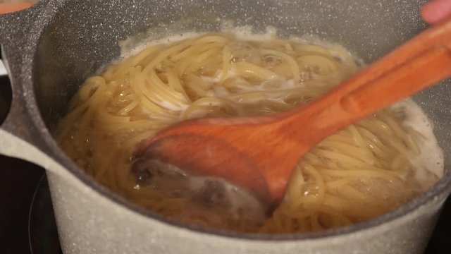 Spaghetti Al Dente Cooking On Steel Pan In Slow Motion Close Up.Pasta Boiled In Boiling Water In A Pan.Italian Cuisine.Close Up Spaghetti In Boiling Water.Linguine Cooked In A Pan.