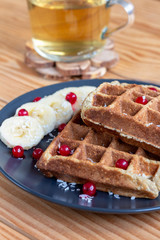 Belgian waffles with red berries and bananas on a wooden background