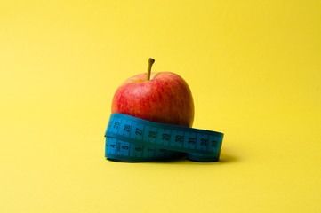 Red apple and a centimeter on a yellow background. The concept of ideas, weight loss and proper nutrition