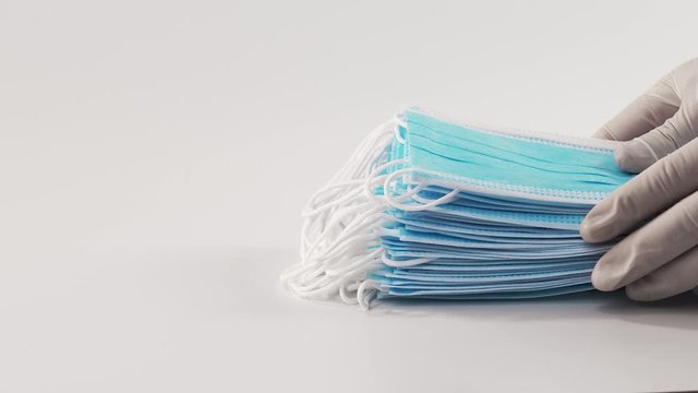 Medical mask on a white background. Nurses' hands place a stack of medical masks on a white sterile surface.
