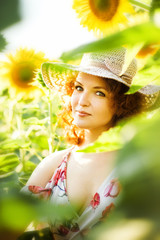 Vertical close-up portrait of young beautiful red haired woman in straw hat in sunflowers field in back light. Summer countryside concept. Close to nature vacation. Woman and sunflowers. Summer light.