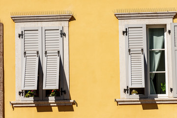 Fototapeta na wymiar Two windows with grey wooden shutters with spike steel sticks to prevent birds from stopping, especially pigeons, residential building in Trentino, Italy, Europe