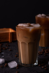 Iced coffee in a tall glass with cream poured over. Wood background. Low key.