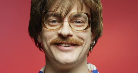Funny retro style dark-haired Caucasian man with mustache and eyeglasses smiling to camera. Close up portrait of happy male over pink background. Vintage stylish model with smile on face. 70s concept