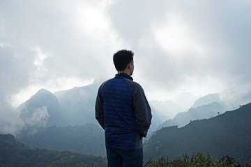 A man standing on the peak looking at green mountain range with cloudy sky