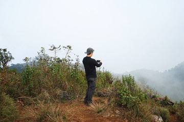 Naklejka premium A man on the peak taking a photo of green mountain range with cloudy sky