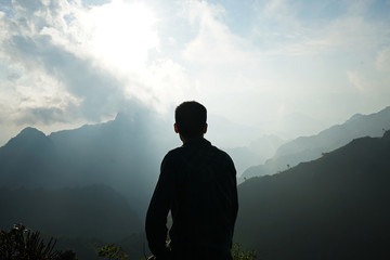 A man standing on the peak looking at green mountain range with cloudy sky