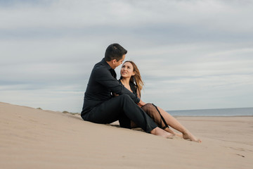 pareja de enamorados sentados en la arena en la playa con el mar de fondo y el cielo y las...