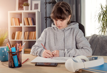 Female teenager studying at home writing or drawing something sitting at table, front view