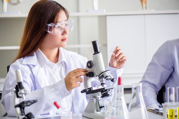 Attractive young Asian scientist woman lab technician assistant analyzing sample in test tube at laboratory. Medical, pharmaceutical and scientific research and development concept.