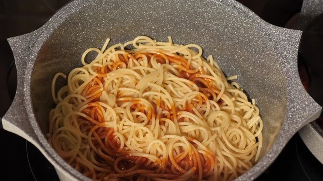 Cooking and stirring the spaghetti with red tomato sauce in the frying pan, close-up 
