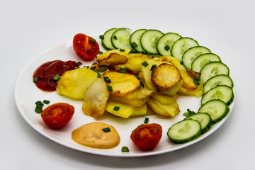 Homemade fried potatoes with fresh cucumbers, cherry tomatoes and sauces on the white plate. Delicious ukrainian fried potatoes with vegetables against background. Cooked tasty meal for lunch.