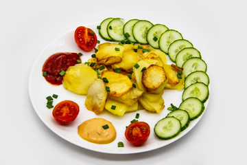 Homemade fried potatoes with fresh cucumbers, cherry tomatoes and sauces on the white plate. Delicious ukrainian fried potatoes with vegetables against background. Cooked tasty meal for lunch.