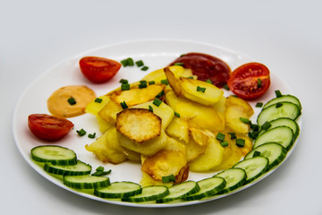 Homemade fried potatoes with fresh cucumbers, cherry tomatoes and sauces on the white plate. Delicious ukrainian fried potatoes with vegetables against background. Cooked tasty meal for lunch.