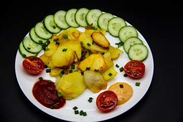 Homemade fried potatoes with fresh cucumbers, cherry tomatoes and sauces on the white plate. Delicious ukrainian fried potatoes with vegetables against background. Cooked tasty meal for lunch.