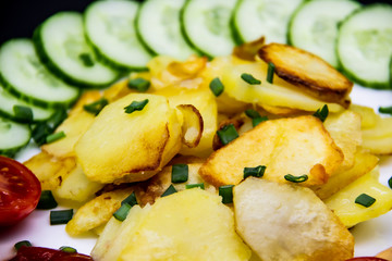 Homemade fried potatoes with fresh cucumbers, cherry tomatoes and sauces on the white plate. Delicious ukrainian fried potatoes with vegetables against background. Cooked tasty meal for lunch.