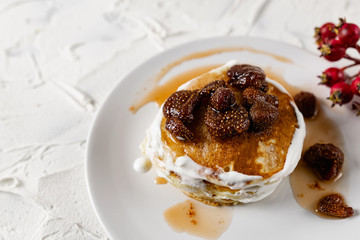 A stack of crumpets and pancakes with sour cream and strawberry sweet jam with berries on top of the dish. Dessert on a white plate with fruit in the background.