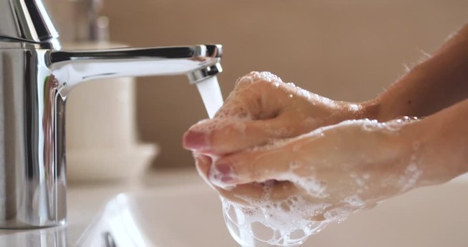 Close up shot of an young woman applying soap while washing hands for hygiene purpose in washbowl with open tap. Concept of personal hygiene, cleanliness, sanitary, disinfection