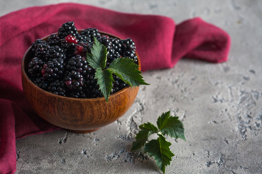 Sweet blackberry and leaves in wooden bowl on grey stone background.