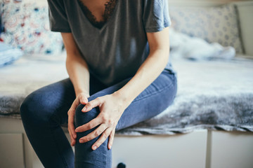 Woman suffering from knee pain while sitting on bed.