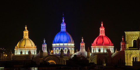 The domes of the New Cathedral in Cuenca, Ecuador light up at sunset in the colors of the...