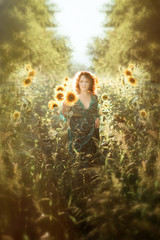 Vertical portrait of young beautiful red haired woman in long green dress walking in sunflowers field in back light. Summer countryside concept. Close to nature vacation. Woman and sunflower. Summer