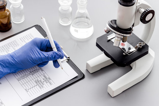 Bood testing with microscope in laboratory. Hand writes results. Grey background