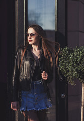 fashionable lady in a leather jacket and sunglasses poses in an urban setting