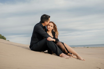 Pareja feliz sentada en la playa, relajados, casual, elegante, vestidos de negro, beso en la...
