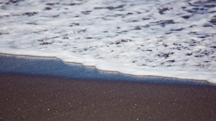 White ocean foam on black sand.