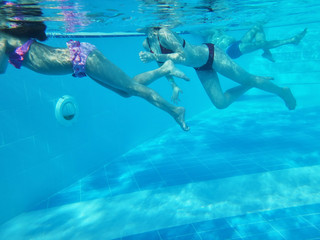 Bodies of mother and small daughter swimming in a pool under water. Woman and girl. Blue color