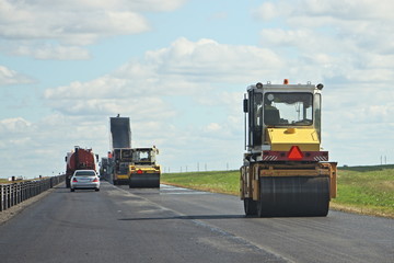 Highway road repair, asphalt laying roller paver on Sunny summer day on blue sky and green field backgroundclothing
