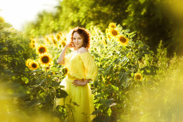 Portrait of young beautiful red haired woman with one hand up in yellow dress in sunflowers field in back light. Summer countryside concept. Close to nature vacation. Woman and sunflowers. Summer