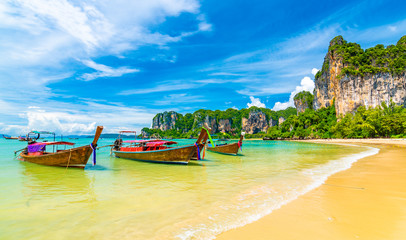 Fototapeta na wymiar Beautiful view of long tail boats on water in Railay beach bay, Thailand, Krabi town. Famous tourist destination for vacation in tropical paradise. Beautiful summer day. Big limestone hill and rock