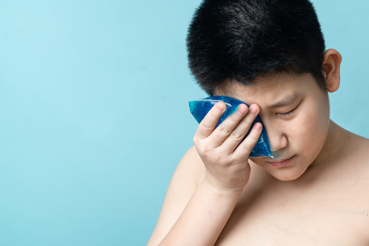 Asian preteen boy using cold compress gel on bruises face on blue background.